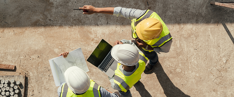 Personnes sur chantier avec un plan, un ordinateur portable qui discute