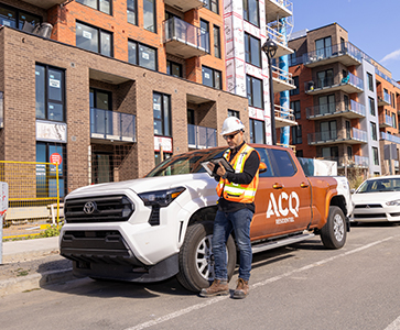 surveillant de chantier avec une tablette devant un camion de l'ACQ Résidentiel