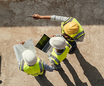 Personnes sur un chantier avec un plan et ordinateur portable qui discute